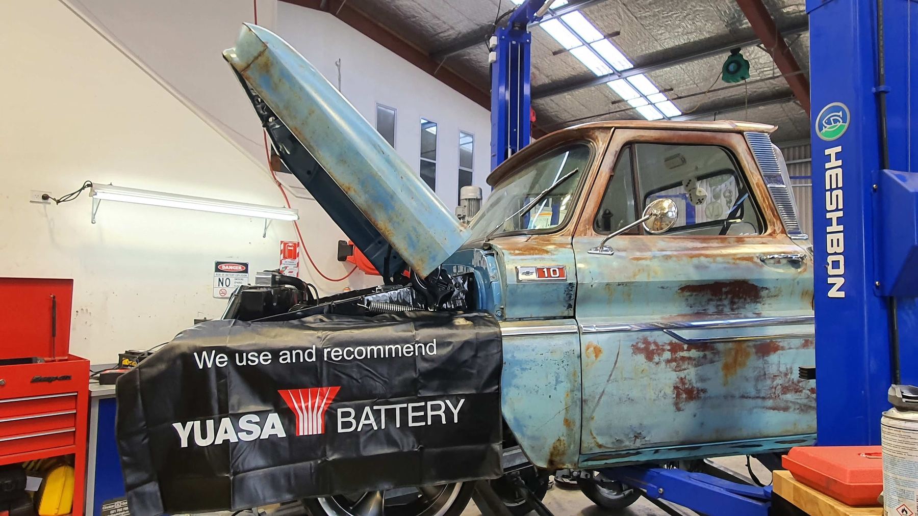 A vehicle up on the hoist inside the Motorworks workshop, beside a Yuasa battery bench cover